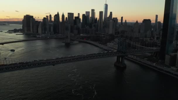 Εναέρια πλάνα μεγάλων κρεμαστών γεφυρών πάνω από το ανατολικό ποτάμι μετά το ηλιοβασίλεμα. Γείρε ψηλά αποκαλύπτοντας τον ορίζοντα με τους σύγχρονους ψηλούς ουρανοξύστες του κέντρου ενάντια στον πολύχρωμο ουρανό. Μανχάταν, Νέα Υόρκη, ΗΠΑ — Αρχείο Βίντεο