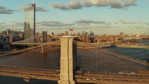 Amerikai zászló a Brooklyn híd tetején. Festői légi felvétel hidakról és épületekről a városban, napnyugtakor megvilágítva. Manhattan, New York City, Amerikai Egyesült Államok — Stock videók