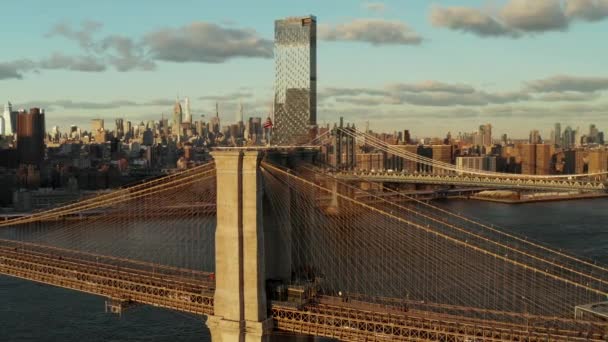 Aerial view of historic cable stayed bridge over river. Brooklyn Bridge and cityscape in background lit by late afternoon sun. Manhattan, New York City, USA — Stock Video