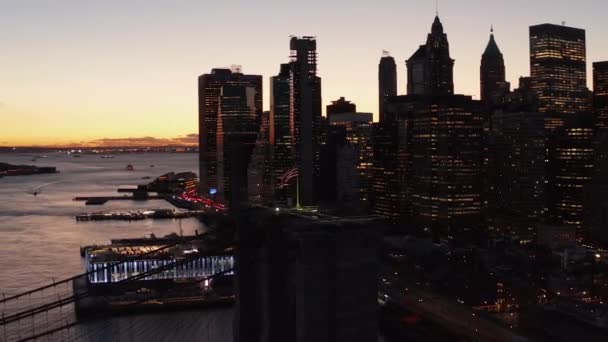 Orbit shot around American flag on top of suspension tower of Brooklyn bridge. Panning shot of city at dusk. Skyscrapers against sunset sky. New York City, USA — Vídeo de Stock