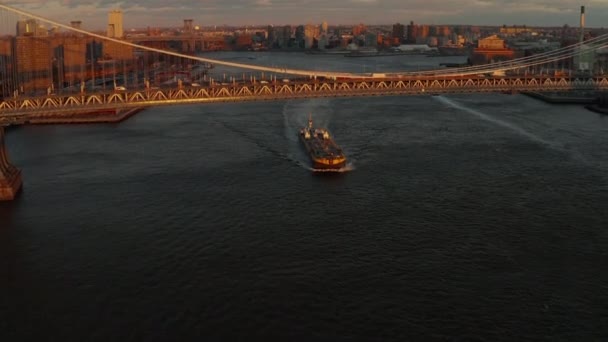Μεγάλο φορτηγό πλοίο περνάει κάτω από πολυσύχναστη γέφυρα του Μανχάταν το ηλιοβασίλεμα. Δομή γέφυρας φωτισμένη από τις τελευταίες ακτίνες του ήλιου. Μπρούκλιν, Νέα Υόρκη, ΗΠΑ — Αρχείο Βίντεο