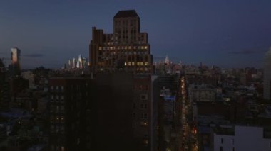 Günbatımından sonra şehrin üzerinde uçuyor. Karanlık gökyüzüne karşı ışıklı pencereleri olan büyük bir ofis binası. Manhattan, New York City, ABD