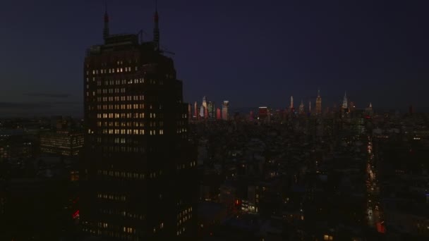 Fly above night city. Passing by tall office building with lighted windows. Revealing panoramic view of illuminated downtown skyscrapers in distance. Manhattan, New York City, USA — Vídeo de Stock