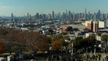 İleri, tarihi Calvary Mezarlığı 'nın ve kasabanın etrafındaki ilçenin üzerinden uçuyor. Arka planda modern yüksek binalar var. New York City, ABD