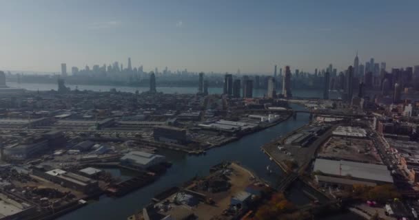 Fly above industrial borough, logistic or production facilities along Newtown Creek water transport way. Manhattan business skyscrapers in distance. New York City, USA — стоковое видео