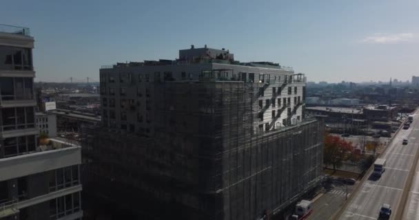 Fly over apartment building with rooftop terraces and scaffolding around facade. Revealing multilane expressway and panoramic view of industrial or logistic site. New York City, USA — Stockvideo