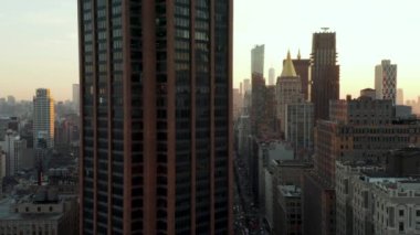Şehirdeki yüksek binaların etrafında uç. Gün batımına karşı şehir merkezindeki gökdelenlerle gökyüzü aydınlanıyor. Manhattan, New York City, ABD