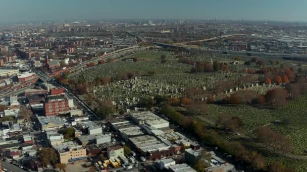 Aerial panoramic view of large city. Highway interchange near large Calvary Cemetery. Tilt down on rows of tombstones in green lawn. Queens, New York City, USA — стокове відео