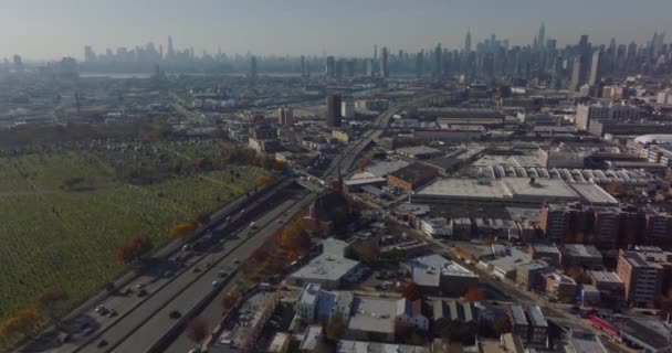Aerial panoramic shot of large city. Busy multilane expressway leading along cemetery. Downtown skyscrapers in distance. Queens, New York City, USA — Stock Video