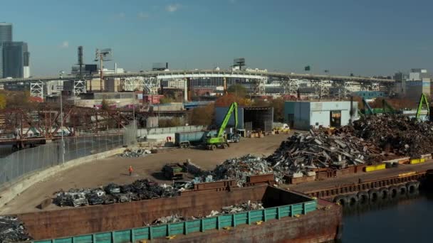 Slide and pan footage of loader moving on scrap yard on Newtown Creek waterfront. Piles of used metal material for recycling. Busy elevated road in background. New York City, USA — стоковое видео