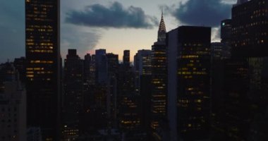 Şehir merkezindeki yüksek binaların yükselişi. Aydınlatılmış pencereler ve çatıdaki renkli ışık süslemeleri alacakaranlık gökyüzüne karşı. Manhattan, New York City, ABD