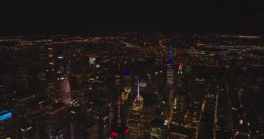 İleri uçaklar gece şehrin üzerinde uçar. Renkli kulelerle aydınlatılmış gökdelenler. Manhattan, New York City, ABD