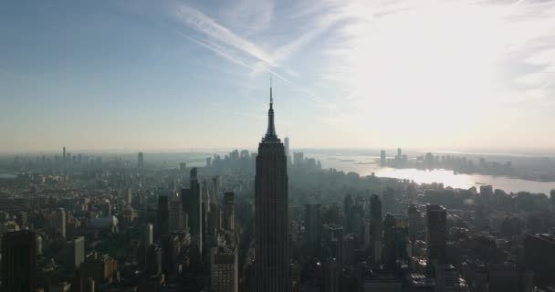Letecký pohled na Empire State Building tyčící se vysoko nad okolním vývojem. Cityscape s mrakodrapy v centru města proti jasné obloze. Manhattan, New York City, USA — Stock video