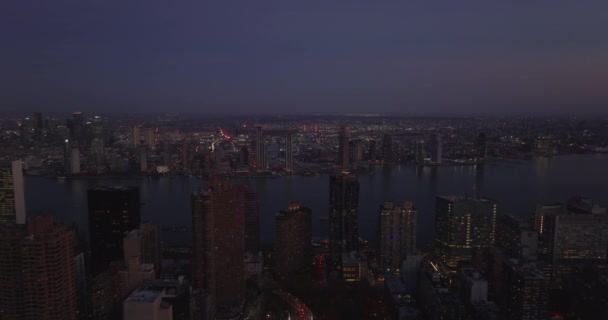 Avante voar acima da cidade após o pôr do sol. Vista aérea de largo East River rodeado por edifícios de arranha-céus em frentes de água. Manhattan, Nova Iorque, EUA — Vídeo de Stock