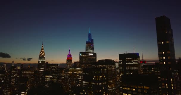 Sestupné záběry výškových budov s osvětlenými okny. Ikonické mrakodrapy v centru města proti barevné obloze za soumraku. Manhattan, New York City, USA — Stock video