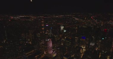 Gece şehrinin üzerinde uç. Şehir merkezinde uzun gökdelenler ve binalar var. Kasaba semtlerinde binlerce ışık var. Manhattan, New York City, ABD