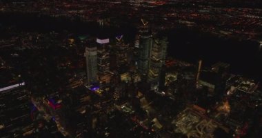 İleri uçaklar gece şehrin üzerinde uçar. Yüksek apartmanlardan oluşan aydınlanmış bir grup. Manhattan, New York City, ABD