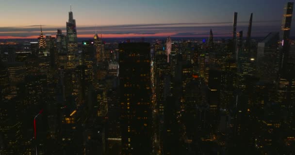 Imágenes aéreas descendentes de la noche en el centro. Rascacielos modernos y edificios de gran altura con ventanas iluminadas contra el cielo colorido. Manhattan, Nueva York, Estados Unidos — Vídeo de stock
