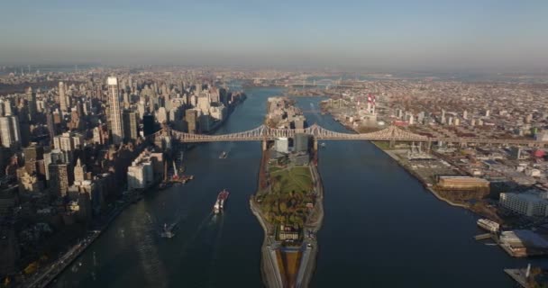 Panoramisch uitzicht vanuit de lucht op Roosevelt Island en de lange Queensboro Bridge. Vrachtschepen drijvend op East River in de late namiddag. Manhattan, New York City, Verenigde Staten — Stockvideo