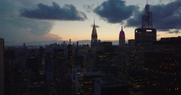A frente voa acima da cidade ao entardecer. Topos iluminados de arranha-céus icônicos. Chrysler e Empire State Building contra o pôr-do-sol. Manhattan, Nova Iorque, EUA — Vídeo de Stock