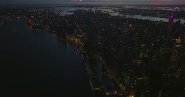 Fly above East River bank in evening. Tilt up reveal cityscape against colourful twilight sky. Manhattan, New York City, USA — Stock Video