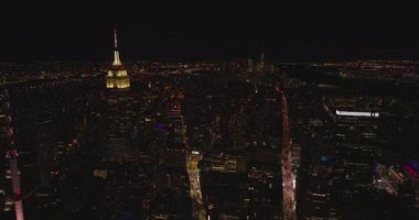 İleri, gece kasabasının üzerinde uçar. Görkemli Empire State Binası 'nın en üst bölümü ve kulesi aydınlatıldı. Manhattan, New York City, ABD