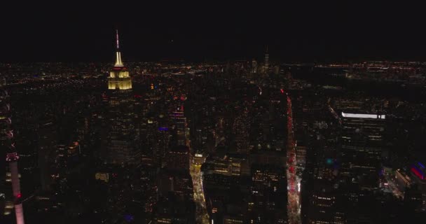 Adelante vuelan por encima de la ciudad nocturna. Sección superior iluminada y aguja del majestuoso Empire State Building. Manhattan, Nueva York, Estados Unidos — Vídeo de stock