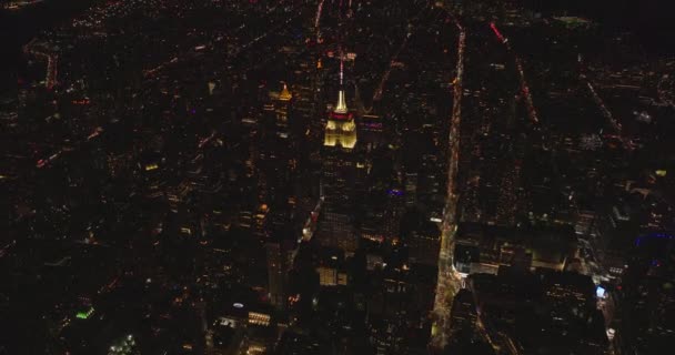 Empire State Building with illuminated top section and spire. Tilt up reveal of night cityscape. Manhattan, New York City, USA — 图库视频影像