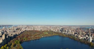 Idyllic sonbahar günü. Etrafında su deposu ve binalar olan renkli Central Park 'ın havadan görünüşü. Açık mavi gökyüzü. Manhattan, New York City, ABD