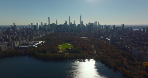 Aerial descending footage of water reservoir, softball fields and autumn trees in Central Park surrounded by high rise buildings. Manhattan, New York City, USA — Stockvideo