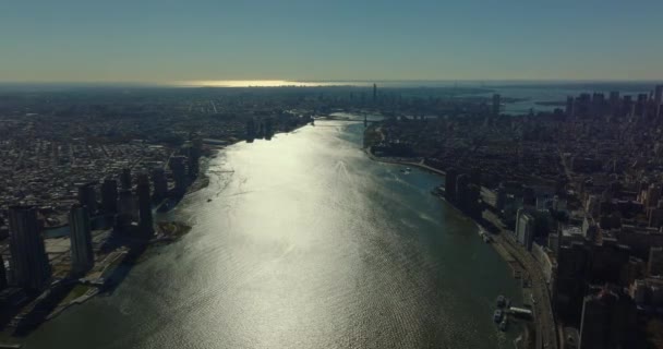 Terbang tinggi di atas sungai Timur melewati antara distrik kota. Permukaan air memantulkan sinar matahari. Manhattan, New York City, Amerika Serikat — Stok Video