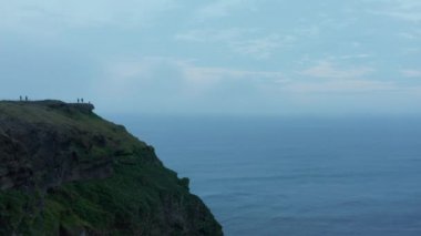 İleri, deniz kıyısındaki dik uçurumun kenarından uçar. İnsanlar gözetleme platformunda eğleniyor. İzlanda