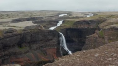 Derin kanyona düşen inanılmaz panoramik su görüntüsü. Kayanın kenarındaki insanlar güzel, korunmuş İskandinav doğasına bakıyorlar. Haifoss, İzlanda