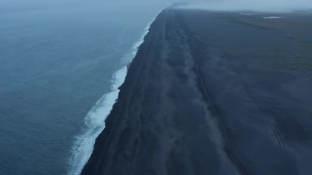Filmato aereo panoramico della costa. Tilt up rivelano di onde lavaggio lunga spiaggia vulcanica nera. Nebbia che limita la visibilità. Paesi Bassi — Video Stock