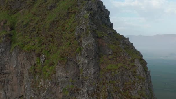 Un affleurement rocheux de haute falaise. Glissant révéler sur une large vallée avec des maisons et de la végétation verte. Islande — Video