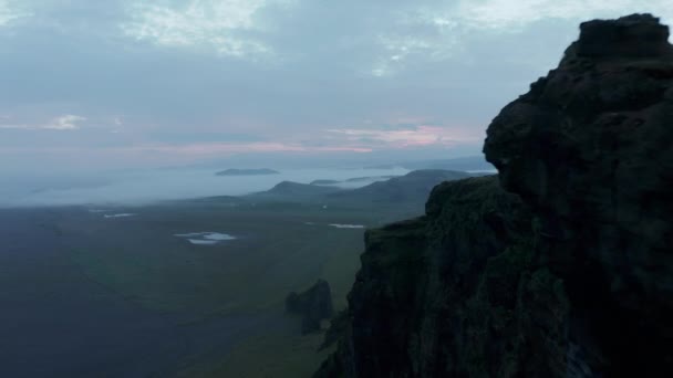 Framåt flyger över kanten av sluttningen. Stryktålig bergvägg ovanför slätten. Morgonlandskap översvämmat av dimma. Island — Stockvideo