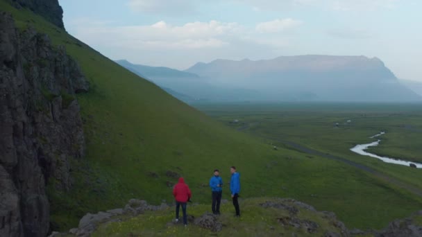 Rückwärts zeigt sich eine Gruppe von Fotografen in einer wunderschönen Landschaft. felsigen Hang mit grünem Gras gewachsen. Nahaufnahme eines fliegenden Vogels. Island — Stockvideo