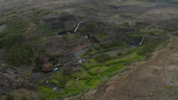 Fantastisk utsikt över ravinen med grön vegetation, strömmande ström och vattenfall kontrasterar mot omgivande karga vulkaniska landskap. Island — Stockvideo