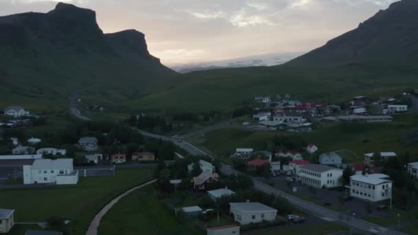 Filmato aereo di strada che conduce tra case in campagna. Montagne contro il tramonto colorato. Villaggio Vik, Islanda — Video Stock