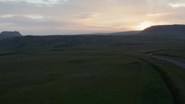 Filmagem panorâmica aérea de carros dirigindo na estrada no campo. Vastas pastagens verdes e colinas vulcânicas. Céu colorido do pôr-do-sol. Islândia — Vídeo de Stock