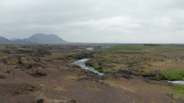 Düz kırsal kesimde akan derenin üzerinden araba geçiyor. Volkanik arazinin üzerinde uç. İzlanda