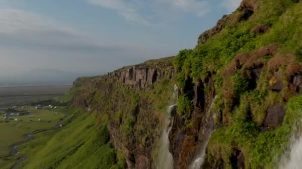 Eng fliegen an hohen Klippen mit Wasserfällen entlang. Grüne Vegetation, die auf Felsen wächst. Schöne Landschaft am Wasserfall Seljalandsfoss. Island — Stockvideo