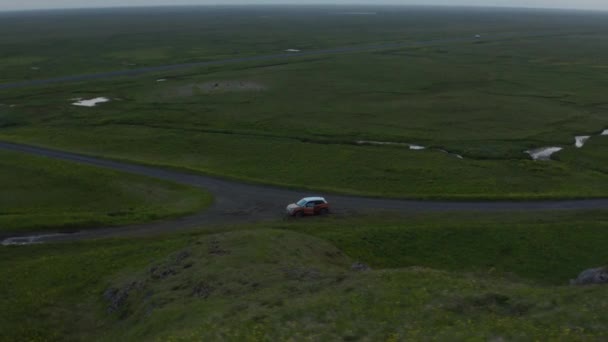 Omloppsbana skjuten runt bilen parkerad vid stigen. Vackert bevarat nordiskt landskap. Grön platt gräsmark kantad av brant stenig sluttning. Island — Stockvideo