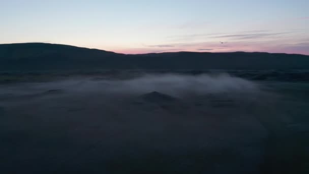 Hacia atrás vuelan por encima del paisaje nebuloso. Silueta de cresta de montaña contra el cielo crepuscular colorido. Pájaro lanzando a través de tiro. Islandia — Vídeos de Stock