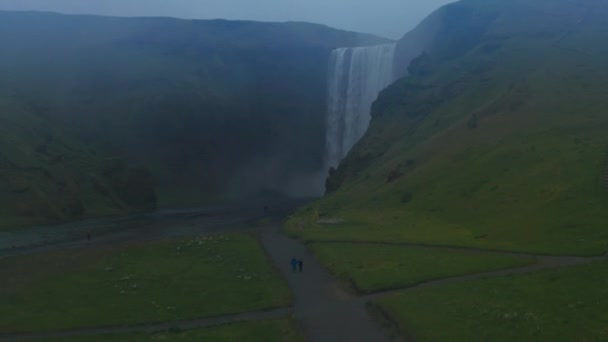 Muhteşem şelalenin yükselen görüntüsü. Vadinin dibinden doğal işaretleri izleyen insanlar. Kuzey 'in puslu kırsal manzarası. İzlanda — Stok video
