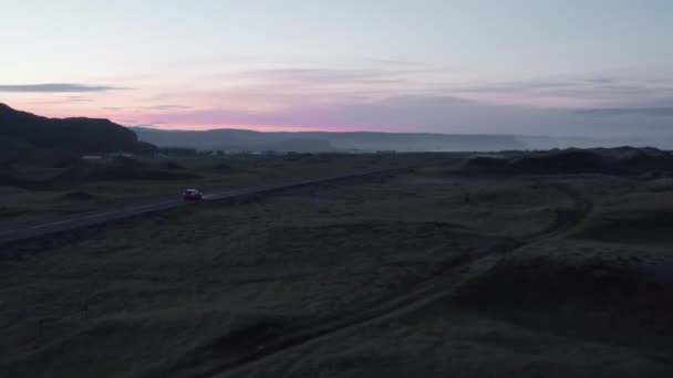 Auto beweegt op de weg door de avond Scandinavische platteland. Romantische kleur schemering hemel op de achtergrond. IJsland — Stockvideo