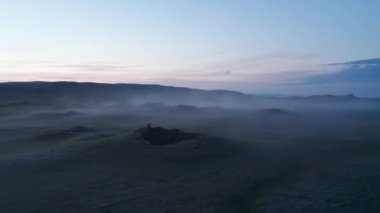 Alacakaranlıkta İskandinav manzarası üzerinde alçak uçuş. Yerden ince bir sis yükseliyor. Renkli alacakaranlık gökyüzü. İzlanda