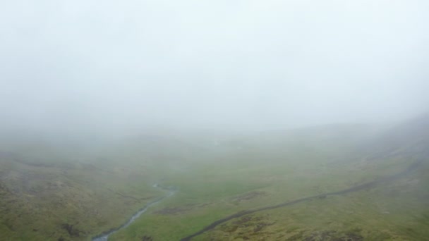 Зеленая трава в долине с горным ручьем. Люди ходят по пешеходной тропе в туманной сельской местности. Исландия — стоковое видео