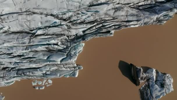 Aves aéreas vista desde arriba hacia abajo vista del frente del glaciar terminando en agua marrón. Hielo de fusión robusto y agrietado iluminado por el sol. Islandia — Vídeo de stock