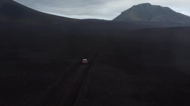 Vista de alto ângulo do carro em movimento na estrada de terra batida no deserto nórdico. Alto cume de montanha à frente. Céu nublado. Islândia — Vídeo de Stock
